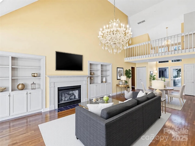 living area with visible vents, a fireplace with flush hearth, an inviting chandelier, and wood finished floors