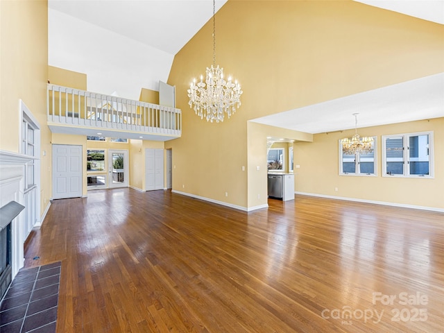 unfurnished living room with baseboards, a chandelier, a fireplace, wood finished floors, and high vaulted ceiling