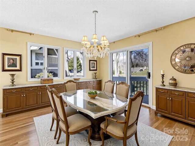 dining area with a notable chandelier, a healthy amount of sunlight, a textured ceiling, and light wood-style floors