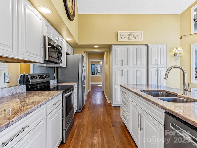 kitchen featuring dark wood-type flooring, light stone counters, appliances with stainless steel finishes, white cabinetry, and a sink