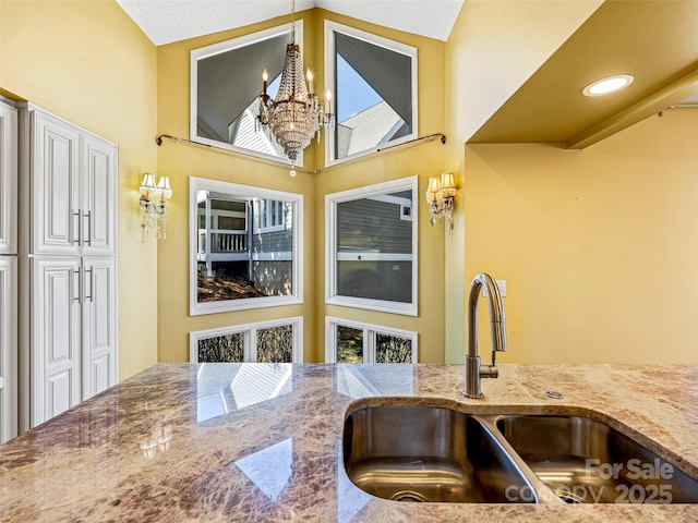 kitchen featuring vaulted ceiling, stone counters, a notable chandelier, white cabinets, and a sink