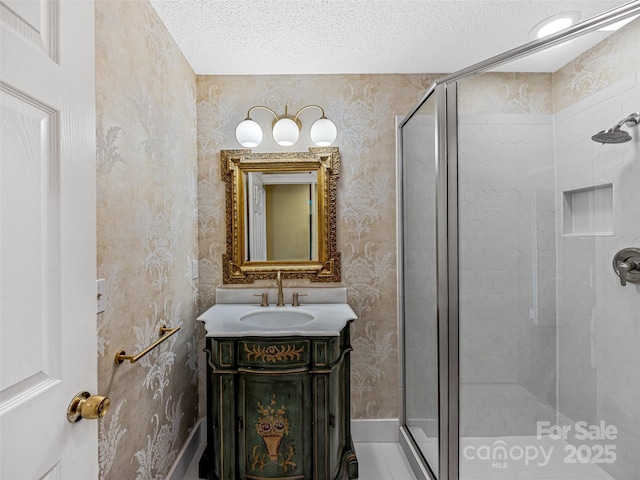 bathroom featuring a shower stall, a textured ceiling, wallpapered walls, and vanity