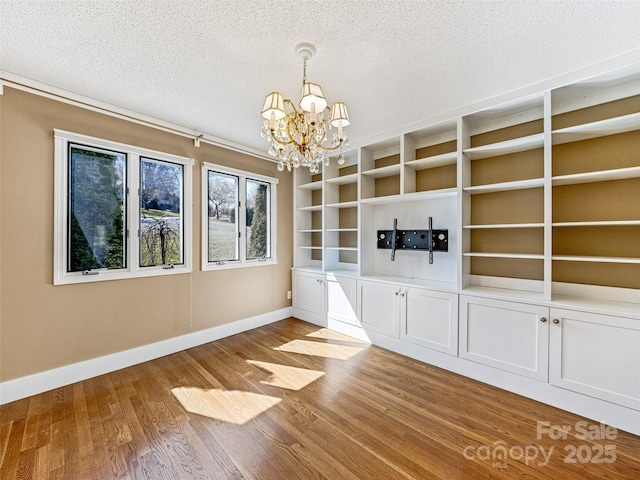 unfurnished dining area with baseboards, a textured ceiling, an inviting chandelier, and wood finished floors