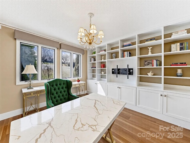 unfurnished dining area featuring light wood-style flooring, a notable chandelier, baseboards, and a textured ceiling