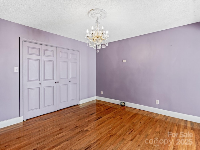 unfurnished bedroom with a textured ceiling, wood finished floors, baseboards, and a chandelier