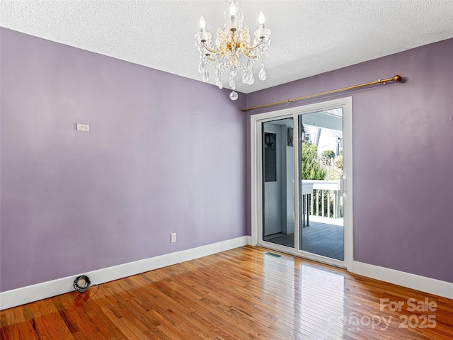 spare room with visible vents, hardwood / wood-style flooring, a textured ceiling, baseboards, and a chandelier