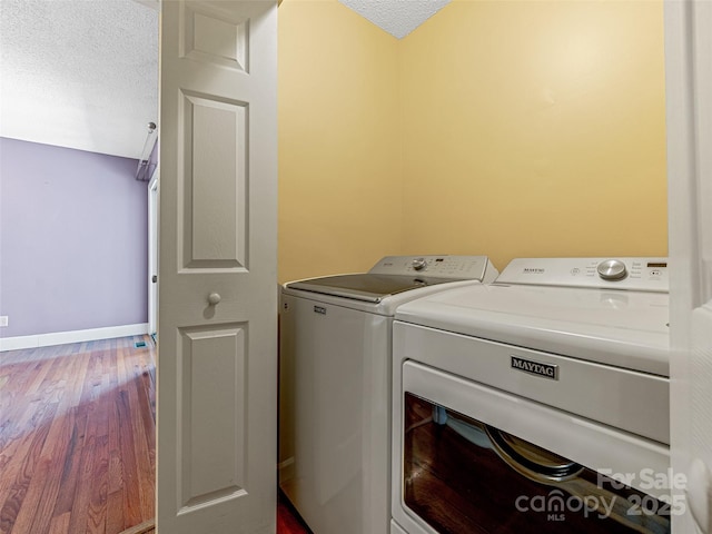 washroom with wood finished floors, baseboards, washing machine and clothes dryer, laundry area, and a textured ceiling