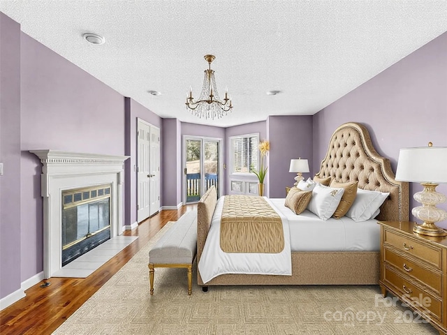 bedroom with baseboards, a chandelier, a fireplace with flush hearth, wood finished floors, and access to outside