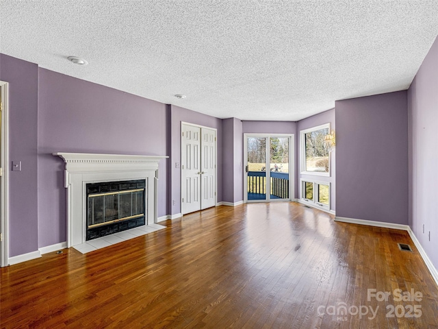 unfurnished living room with visible vents, a fireplace with flush hearth, a textured ceiling, wood-type flooring, and baseboards