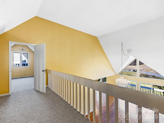 corridor featuring a notable chandelier, carpet floors, baseboards, and vaulted ceiling