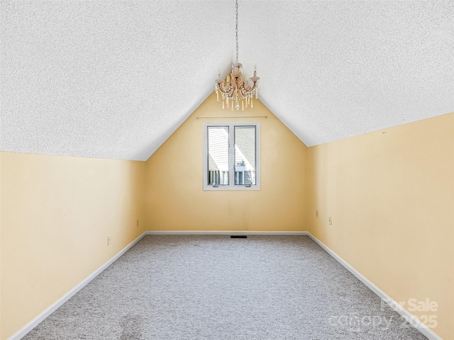 bonus room with baseboards, carpet floors, vaulted ceiling, a textured ceiling, and a notable chandelier