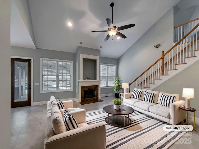 living room with a tiled fireplace, stairway, ceiling fan, and baseboards