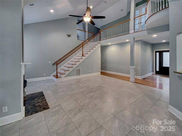 unfurnished living room with visible vents, baseboards, a high ceiling, and stairs