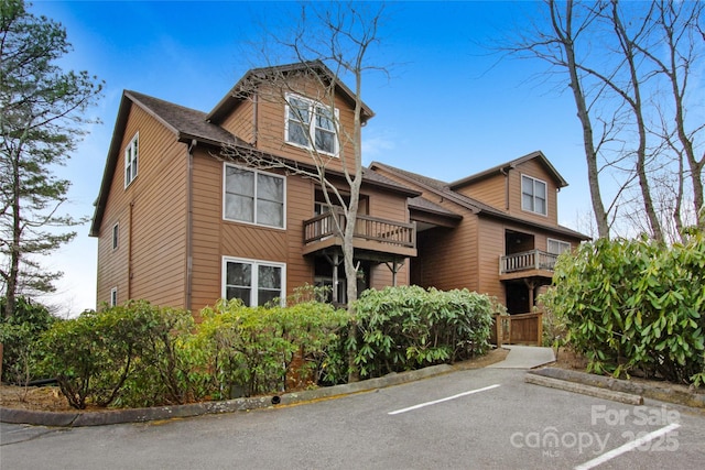 view of front facade with a balcony, uncovered parking, and a shingled roof