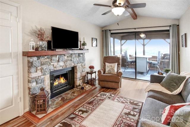 living area featuring a stone fireplace, vaulted ceiling with beams, wood finished floors, and ceiling fan