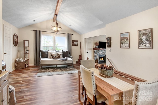 dining area featuring wood finished floors, baseboards, an inviting chandelier, vaulted ceiling with beams, and a stone fireplace