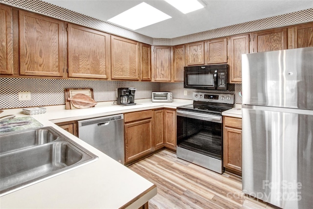 kitchen featuring brown cabinets, decorative backsplash, light countertops, appliances with stainless steel finishes, and light wood-type flooring