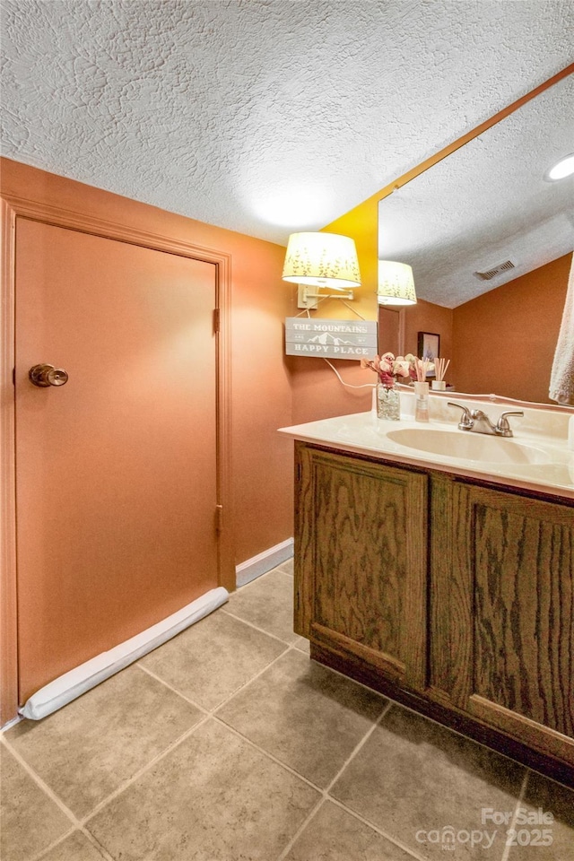 bathroom with tile patterned floors, visible vents, a textured ceiling, baseboards, and vanity