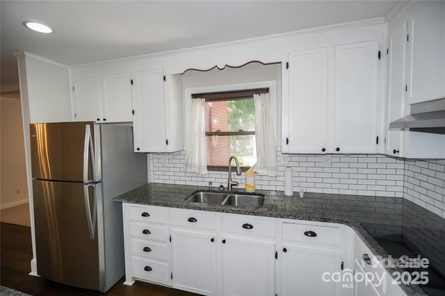 kitchen featuring dark stone countertops, freestanding refrigerator, a sink, white cabinets, and backsplash