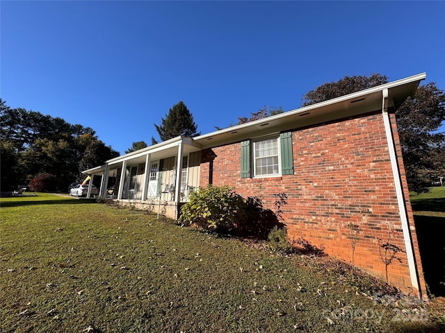 view of side of property featuring a lawn, brick siding, and a sunroom