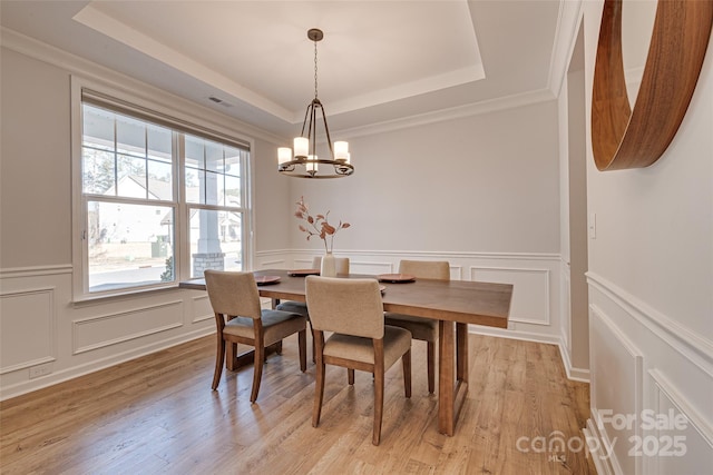 dining area with a tray ceiling, light wood-style floors, visible vents, and a decorative wall