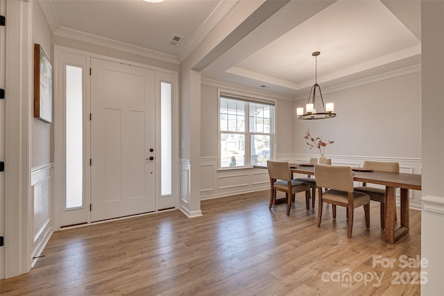 entrance foyer featuring an inviting chandelier, light wood-style flooring, ornamental molding, a raised ceiling, and a decorative wall