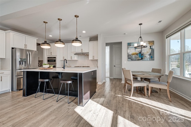 kitchen featuring light wood-style flooring, decorative backsplash, light countertops, white cabinets, and appliances with stainless steel finishes