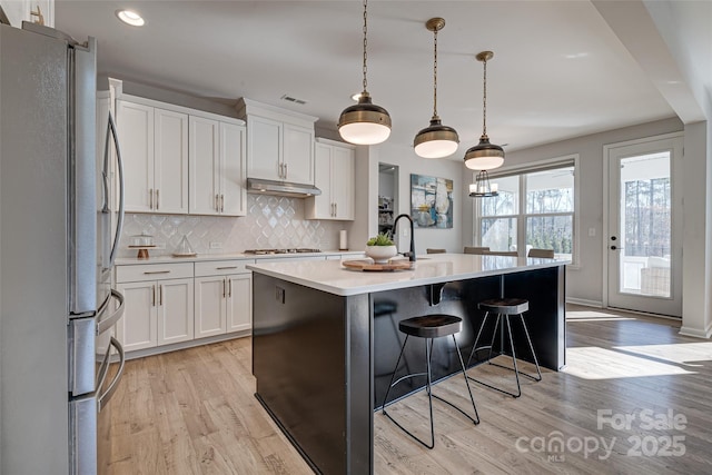 kitchen featuring light wood finished floors, tasteful backsplash, appliances with stainless steel finishes, white cabinets, and light countertops