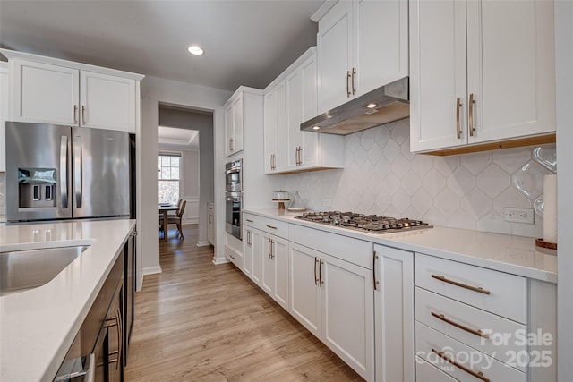 kitchen featuring under cabinet range hood, stainless steel appliances, white cabinets, light wood finished floors, and light countertops