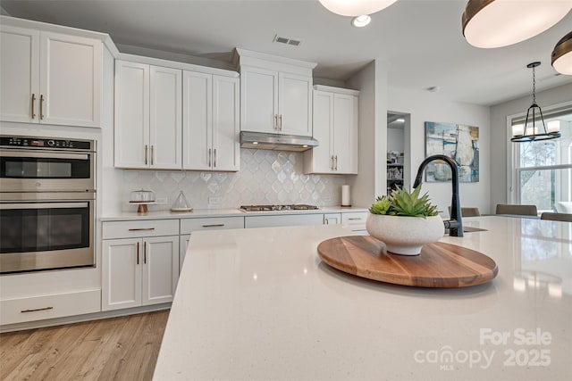 kitchen with pendant lighting, under cabinet range hood, white cabinetry, stainless steel appliances, and light countertops