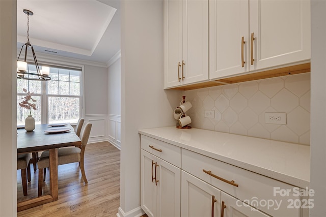 interior space with a wainscoted wall, a tray ceiling, light wood-style flooring, white cabinets, and tasteful backsplash