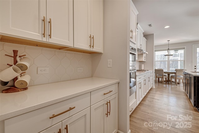 kitchen with light wood-type flooring, recessed lighting, white cabinets, light countertops, and hanging light fixtures