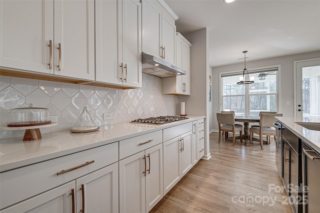 kitchen featuring light wood-type flooring, under cabinet range hood, white cabinetry, appliances with stainless steel finishes, and light countertops