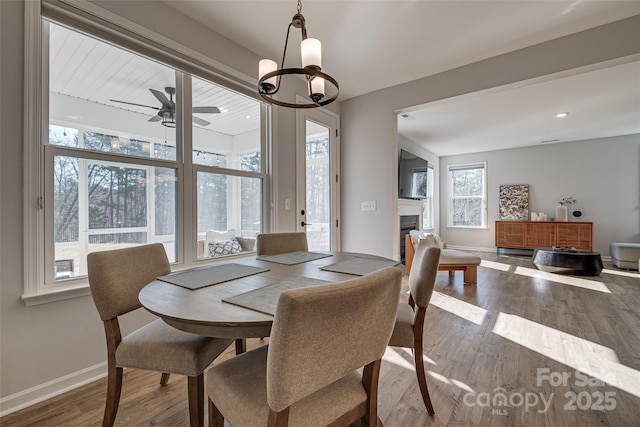 dining room featuring a glass covered fireplace, baseboards, dark wood finished floors, and ceiling fan with notable chandelier