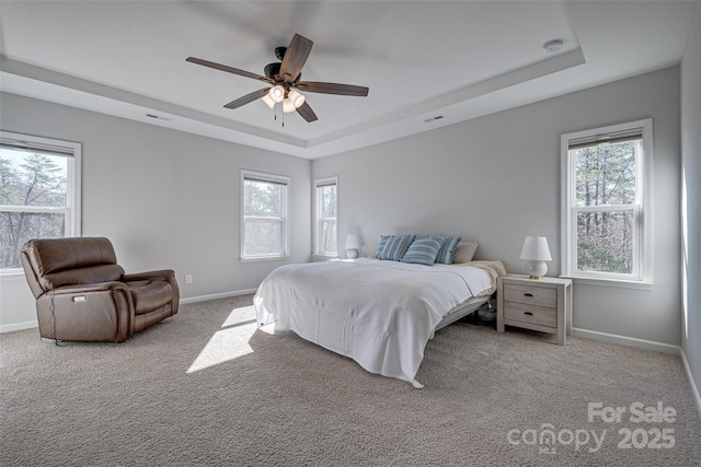 carpeted bedroom with a tray ceiling, baseboards, and multiple windows