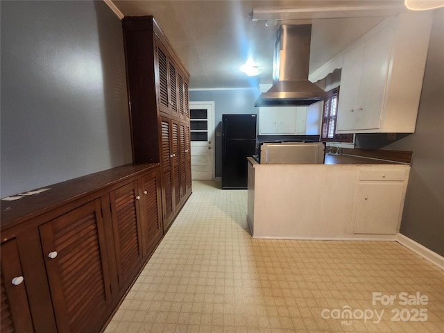 kitchen featuring light floors, a peninsula, freestanding refrigerator, dark countertops, and exhaust hood