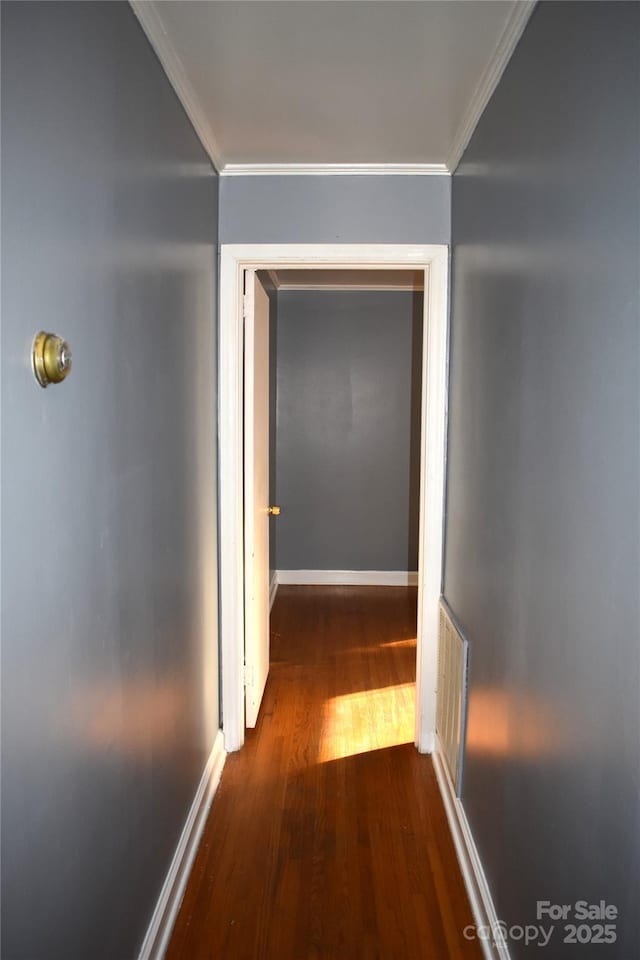 hallway featuring dark wood-type flooring, baseboards, visible vents, and ornamental molding