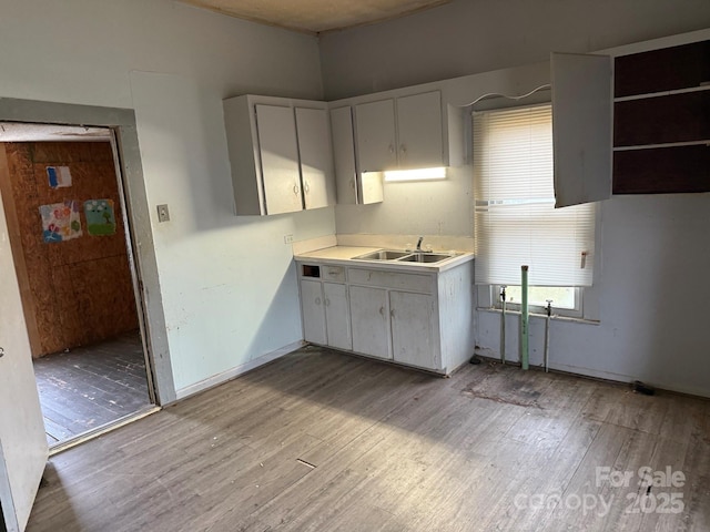 kitchen featuring light countertops, baseboards, light wood finished floors, and a sink