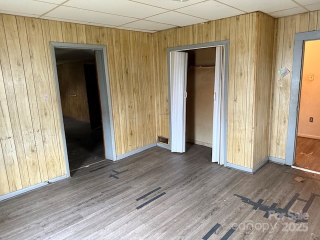 unfurnished bedroom featuring wooden walls, baseboards, a drop ceiling, wood finished floors, and a closet