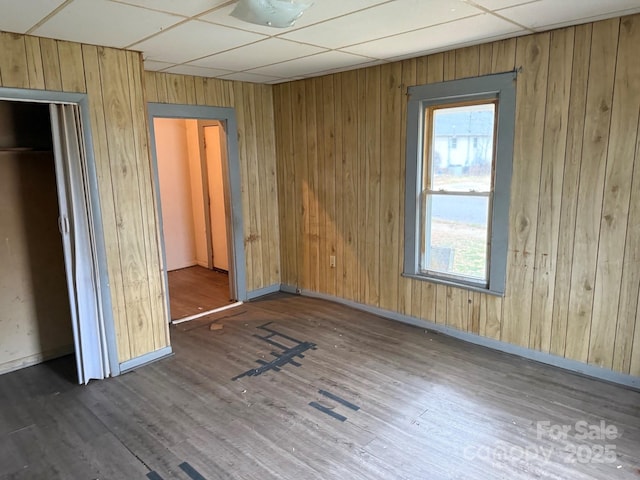 unfurnished bedroom with wooden walls, wood finished floors, baseboards, and a drop ceiling