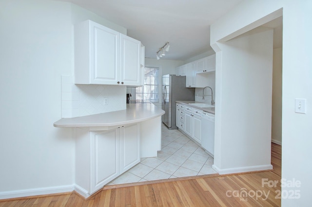 kitchen with tasteful backsplash, dishwasher, light countertops, freestanding refrigerator, and a sink