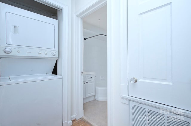 laundry area with stacked washer and dryer and light wood-style flooring