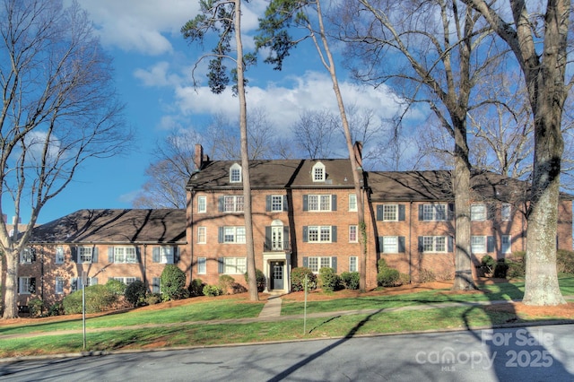 view of front facade with brick siding, a chimney, and a front lawn