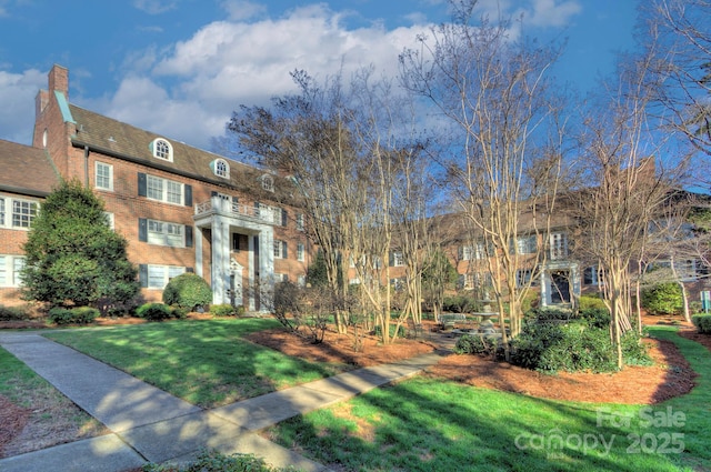 colonial house with brick siding, a chimney, and a front lawn