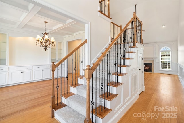 stairway featuring beamed ceiling, a fireplace, hardwood / wood-style flooring, a decorative wall, and coffered ceiling