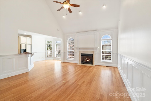 unfurnished living room featuring a wainscoted wall, a fireplace with flush hearth, ceiling fan, light wood-style floors, and a decorative wall