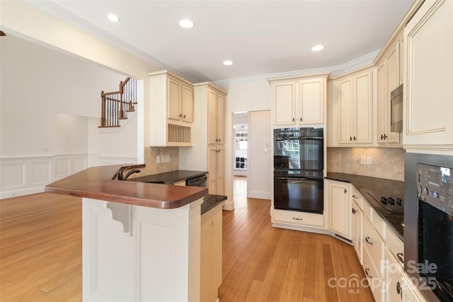 kitchen featuring dark countertops, cream cabinets, and black appliances