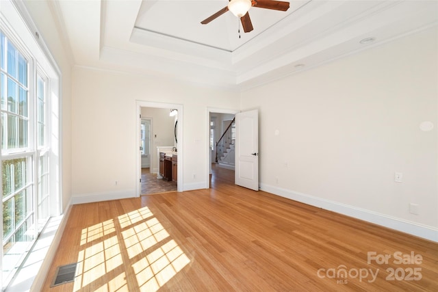 unfurnished bedroom with visible vents, baseboards, a tray ceiling, and light wood-style floors