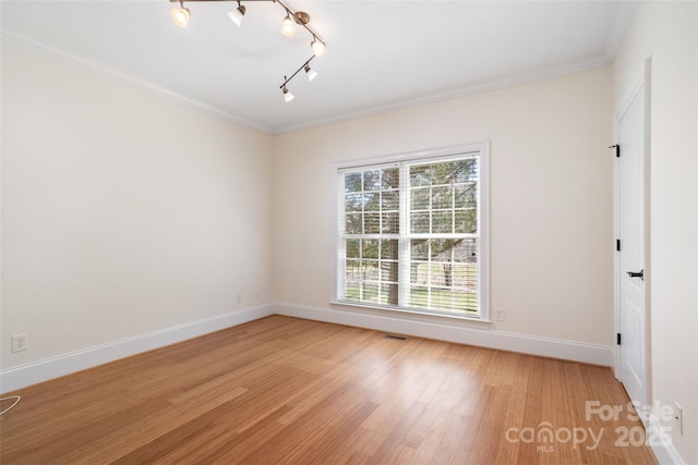 empty room with light wood finished floors, visible vents, baseboards, and ornamental molding