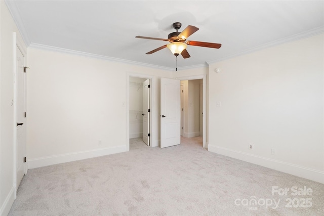 unfurnished bedroom with a ceiling fan, carpet flooring, crown molding, baseboards, and a spacious closet